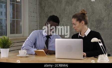 Two colleagues discussing data on laptop putting down notes Stock Photo