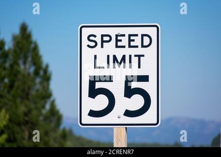 Fifty-five mph speed limit sign on highway. Speed zone traffic sign against blurred tree landscape and blue sky. Stock Photo