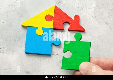 House puzzle Home loan. Parts of the house are brought together. Male hand holding puzzle piece. Stock Photo