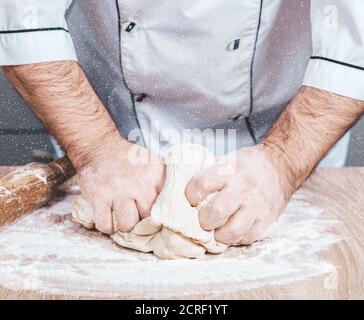 male cook kneads dough on the table, hands close-up Stock Photo