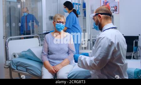 Doctor wearing a visor checking old retired senior woman lungs radiography in modern private hospital clinic. Healthcare facility during COVID-19 global pandemic, wearing protective equipment. Medical care Stock Photo