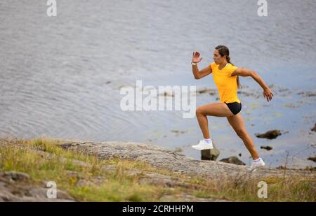 Focused fitness woman doing high-intensity running on mountainside by the sea Stock Photo
