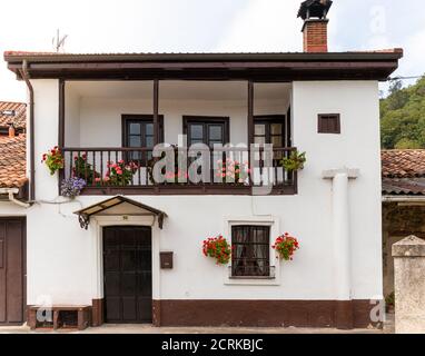 Traditional white house with decorative geranium flowers, typical from Spain. Wooden balcony and windows. Colorful flowers. Chimney on the roof. Astur Stock Photo