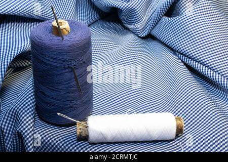 two spools of thread and needles on a piece of tartan Stock Photo