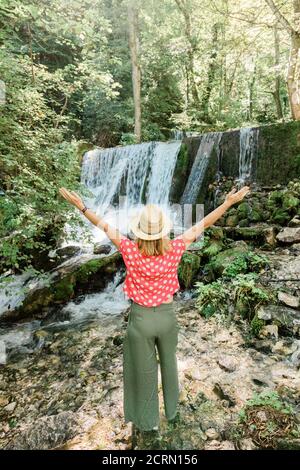 Young female nature explorer standing in front of the waterfall Stock Photo
