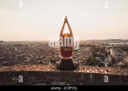 Front view of a back light of a faithful woman in yoga position holding the sun at sunset or sunrise in a beautiful city location with a warm backgrou Stock Photo
