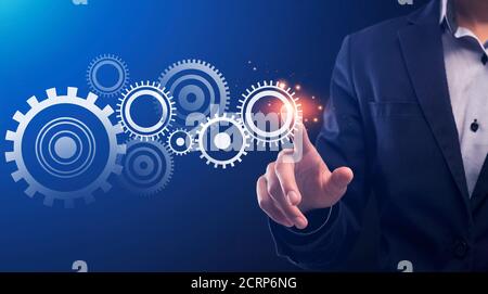 Businessman Pushing Key Starting Cogwheels Mechanism, Blue Background, Conceptual Collage Stock Photo