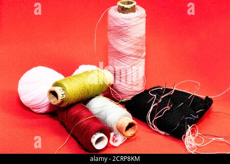 four bobbins of colored threads, two balls of yarn and a needle pad on a red background Stock Photo