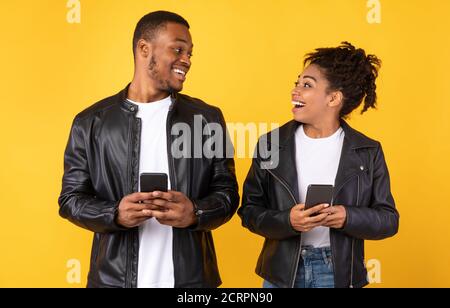 Cheerful African American Couple Using Smartphone Standing Over Yellow Background Stock Photo