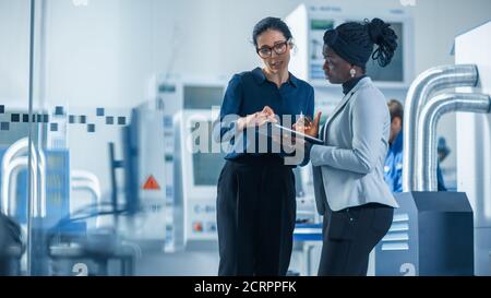Industrial Engineer Talks with Project Supervisor, They Use Digital Tablet Computer and Discuss Modern Factory Planning. Manufacturing Facility with Stock Photo