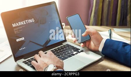 Businessman holding smartphone and using laptop Stock Photo