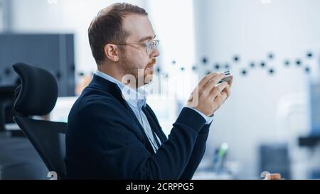 Electronics Factory: Male Electrical Engineer Holds PCB Prototype, Works on Personal Computer. Modern High-Tech Industrial Factory Office. Stock Photo