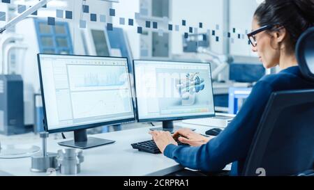 Industrial Female Engineer Working on a Personal Computer, Two Monitor Screens Show CAD Software with 3D Prototype of New Hybrid Hydrogen Engine and Stock Photo
