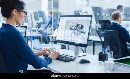 Industrial female Engineer Working on a Personal Computer, Screen Shows CAD Software with 3D Prototype of Engine. Busy Factory with Professional Stock Photo