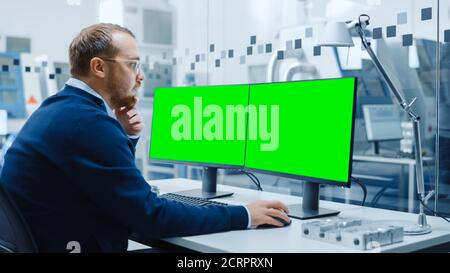 Industrial Engineer Working on a Personal Computer, Two Monitor Screens are Mock-up, Green Screen, Chroma Key Displays. Modern Factory with High-Tech Stock Photo