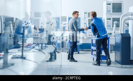 Inside Modern Factory in Facility Workshop Professional Workers Using High-Tech Industrial CNC Machinery, Robot Arm. Professional Industrial Engineer Stock Photo