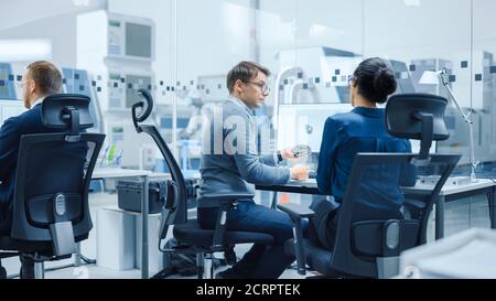 Modern Factory: Female Project Supervisor Talks to a Male Industrial Engineer who Works on Computer. They use CAD Software for Design, Development. In Stock Photo