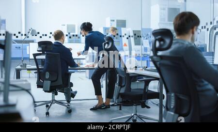 Modern Factory: Female Project Supervisor Talks to a Male Industrial Engineer who Works on Computer. They use CAD Software for Design, Development. In Stock Photo