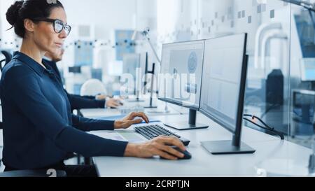 Industrial Engineer Solving Problems, Working on a Personal Computer, Using Mouse and Keyboard, Two Monitor Screens Show CAD Software with Machine Stock Photo