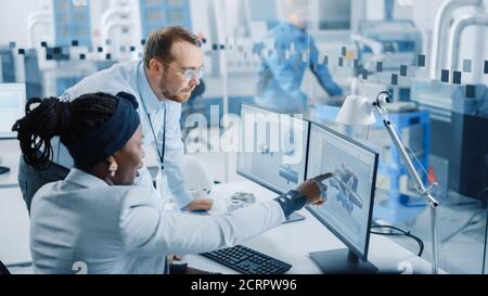 Modern Factory: Male Project Supervisor Talks to a Female Industrial Engineer who Works on Computer. They use CAD Software for Design Hybrid Electric Stock Photo