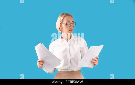 Portrait of serious businesswoman in formal clothes and eyeglasses holding documents over blue studio background Stock Photo