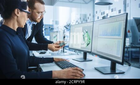 Modern Electronics Factory: Male Supervisor Talks to a Female Electrical Engineer who Works on Computer with CAD Software. Developing PCB, Microchips Stock Photo