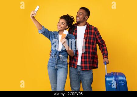 African Couple Making Selfie On Smartphone Holding Tickets, Yellow Background Stock Photo