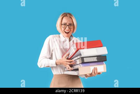 Frustrated office worker overloaded with papers, holding folders of documents on blue studio background Stock Photo