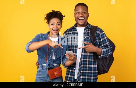 Excited Black Travelers Couple Pointing Finger At Smartphone In Studio Stock Photo
