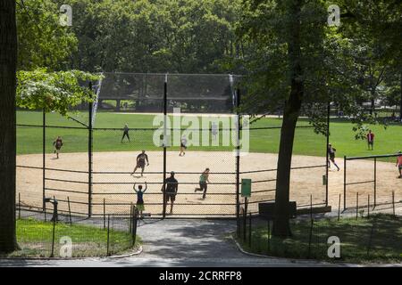 Softball baseball game in Central Park, NYC during the Covid-19 pandemic.  Baseball has natural social distancing built in to the game where the players are spread out on the field. Stock Photo