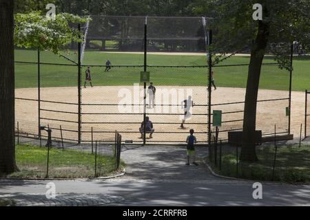 Softball baseball game in Central Park, NYC during the Covid-19 pandemic.  Baseball has natural social distancing built in to the game where the players are spread out on the field. Stock Photo