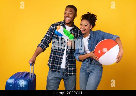 Couple Having Fun Posing With Suitcase And Toys, Yellow Background Stock Photo