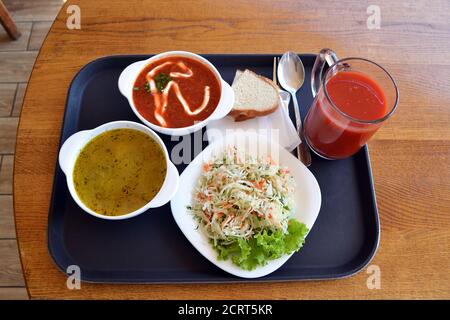 Ukrainian borsh, solyanka, cabbage salad with fresh tomato juice and bread, simple traditional lunch on the wooden table in a local canteen, top view Stock Photo