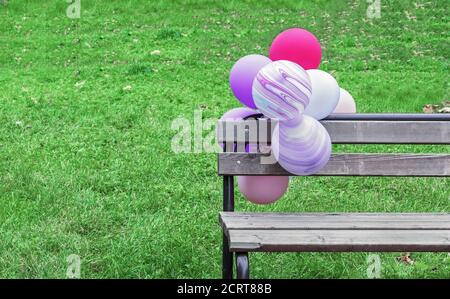 Multicolored balloons on a wooden bench in a city park. Stock Photo