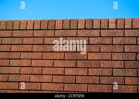 5 - Slanted view of red brick wall on a very bright and sunny day. Red color pops and stands out against the blue sky background. Colorful texture Stock Photo