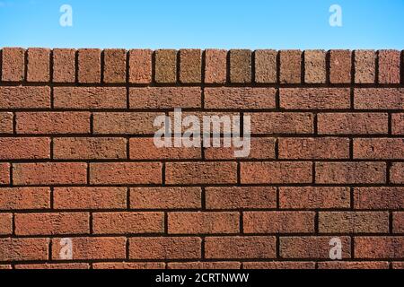 6 - Plain red brick wall background against a bright blue sky background. Sunny summer day. Abstract rough texture with straight dark shadow lines. Stock Photo