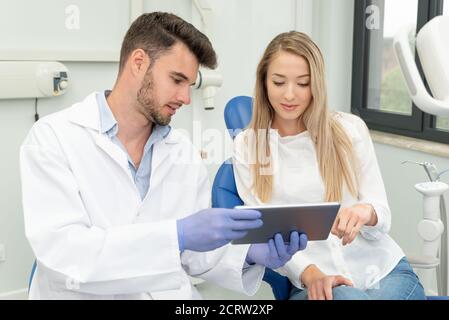 Dental consultation in clinic. Dentist showing teeth x-ray on digital tablet screen Stock Photo