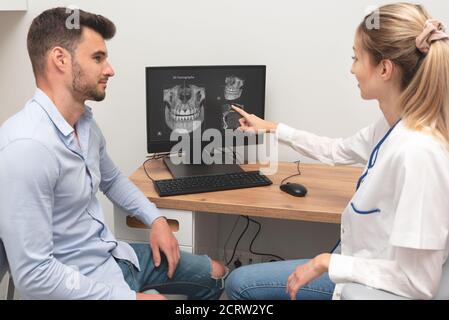 Computer diagnostics dental tomography. Dentist shows the patient an x-ray image at display. Dental care concept. Stock Photo