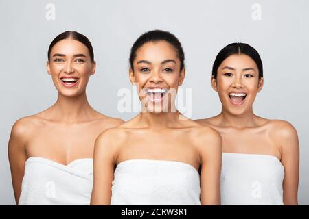 Playful Ladies Posing Wrapped In White Bath Towels, Gray Background Stock Photo