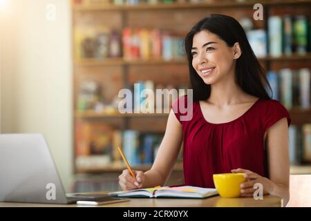 Dreamy Asian Lady Sitting In Cafe, Managing Schedule, Taking Notes To Notepad Stock Photo