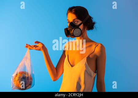 woman in gas mask holding plastic bag with globe on blue, ecology concept Stock Photo