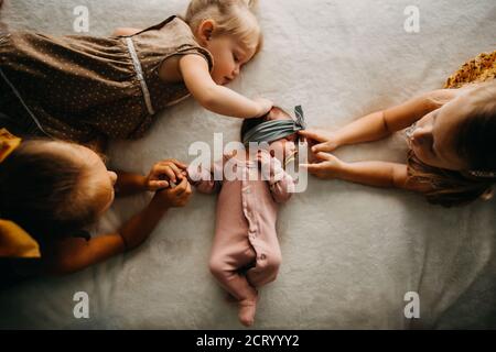 3 sisters laying in bed touching newborn baby girl with pacifier Stock Photo