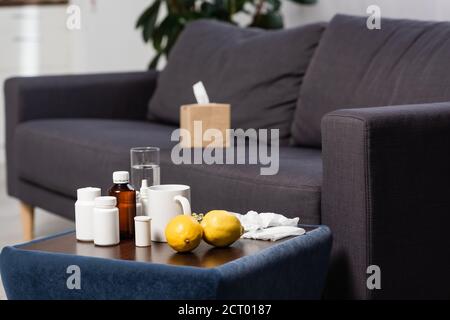 selective focus of medicines, fresh lemons and drinks on bedside table near grey sofa with paper napkins Stock Photo