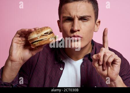 hungry man with hamburgers in hands fast food diet food emotions pink background Stock Photo