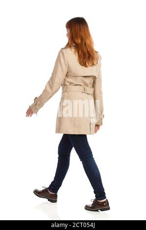 Walking young woman in beige coat, jeans and brown shoes. Rear side view. Full length studio shot isolated on white. Stock Photo