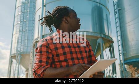 Young handsome african man, engineer using tablet in front of silo system. High quality photo Stock Photo