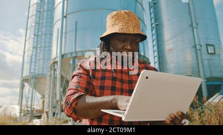 African farmer using laptop in front of the silo storage system. High quality photo Stock Photo