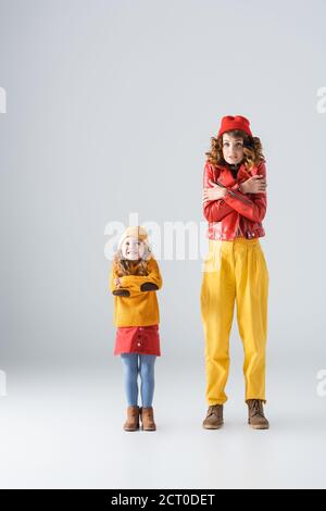 mother and daughter in colorful red and yellow outfits feeling cold on grey background Stock Photo