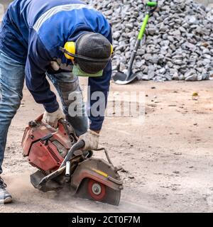 Cutting concrete floor for cable laying using diamond cutting. Construction worker in safety glasses and noise-canceling headphones at work Stock Photo