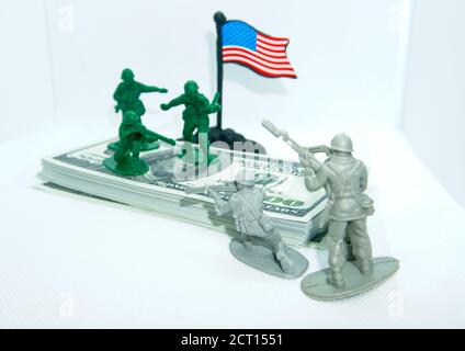 Plastic figures of miniature soldiers in gray and green colors on top of a wad of hundred dollar bills with a U.S. flag on the side with a white backg Stock Photo